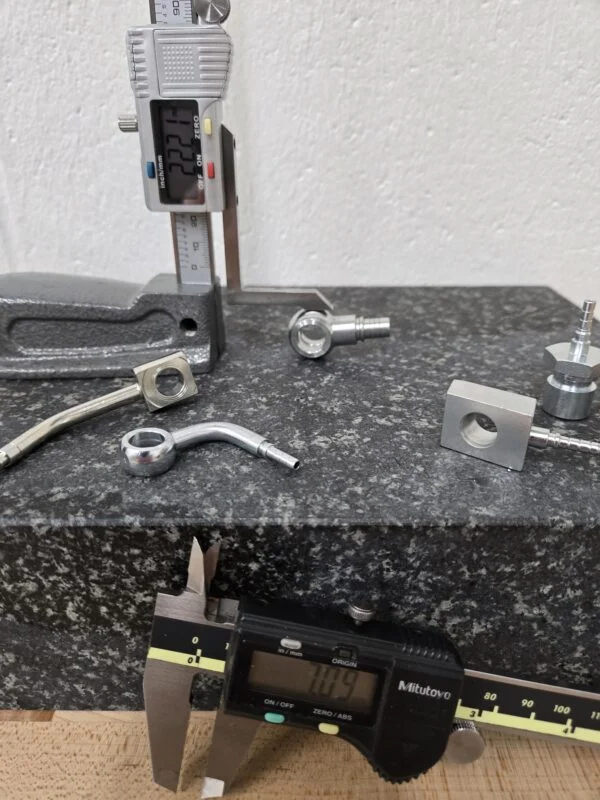 Digital calipers measuring banjo fittings on a granite surface plate